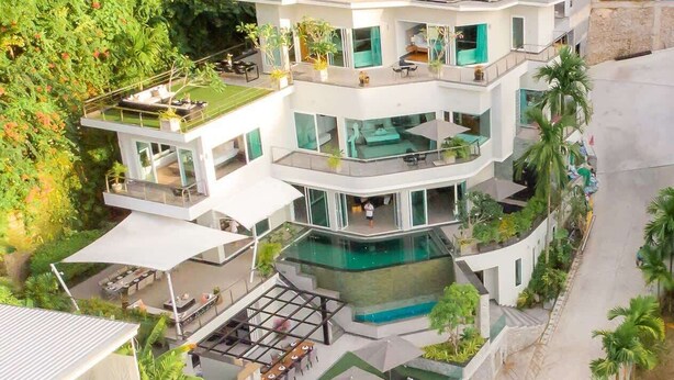 Un immeuble moderne à plusieurs étages, doté de balcons, d’un jardin sur le toit et d’une piscine.
