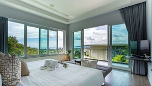 Une chambre d’hôtel moderne dotée d’un grand lit, d’une télévision et d’un balcon offrant une vue sur la ville et la verdure.