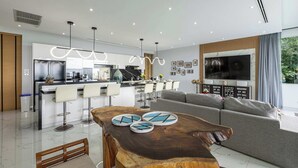 Un salon moderne avec une table basse en bois, un canapé gris et un coin cuisine doté de tabourets de bar blancs.
