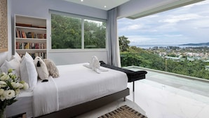 Une chambre moderne avec un grand lit, une bibliothèque et une vue sur le paysage urbain, visible à travers une grande fenêtre.