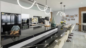 Une cuisine moderne dotée d’un plan de travail en marbre noir, d’un grand îlot central et d’un coin repas avec des chaises blanches.