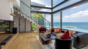 Un salon moderne avec un plancher en bois, un canapé en cuir noir, une table basse et une grande fenêtre donnant sur l’océan.