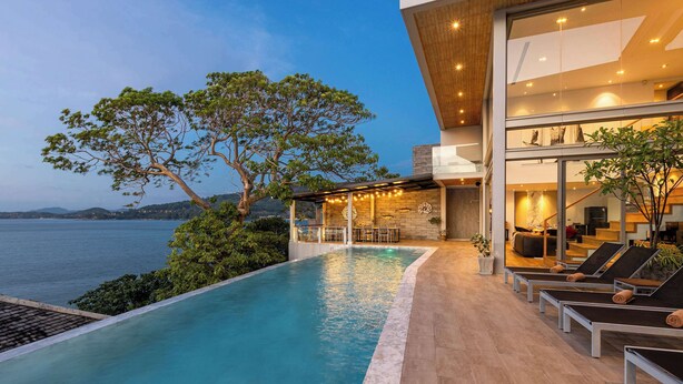 Un espace moderne aménagé au bord de la piscine, avec vue sur la mer, des chaises longues et un coin salon abrité.
