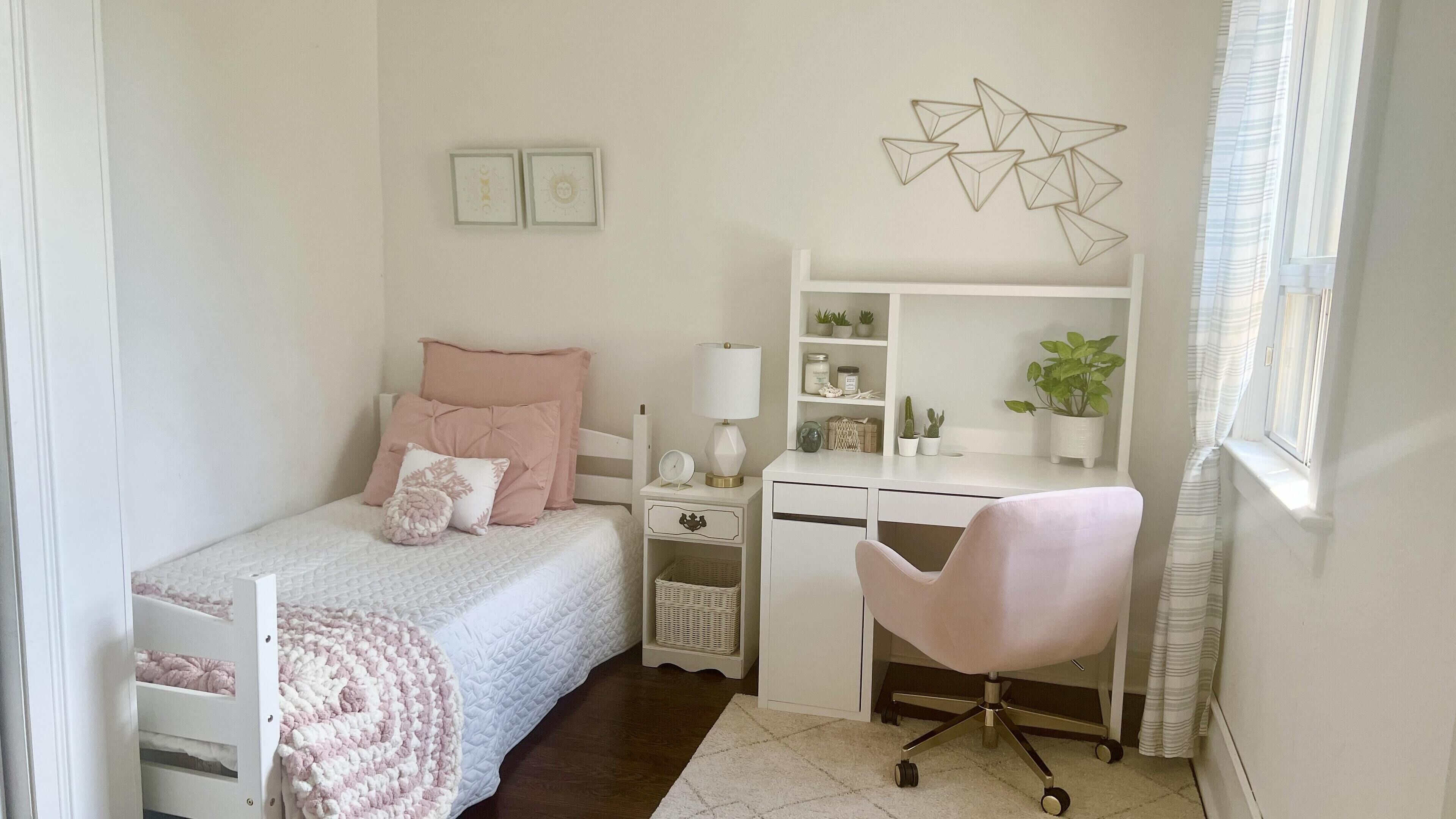 A neatly arranged bedroom with a bed, bedside table, lamp, and a desk with a chair.