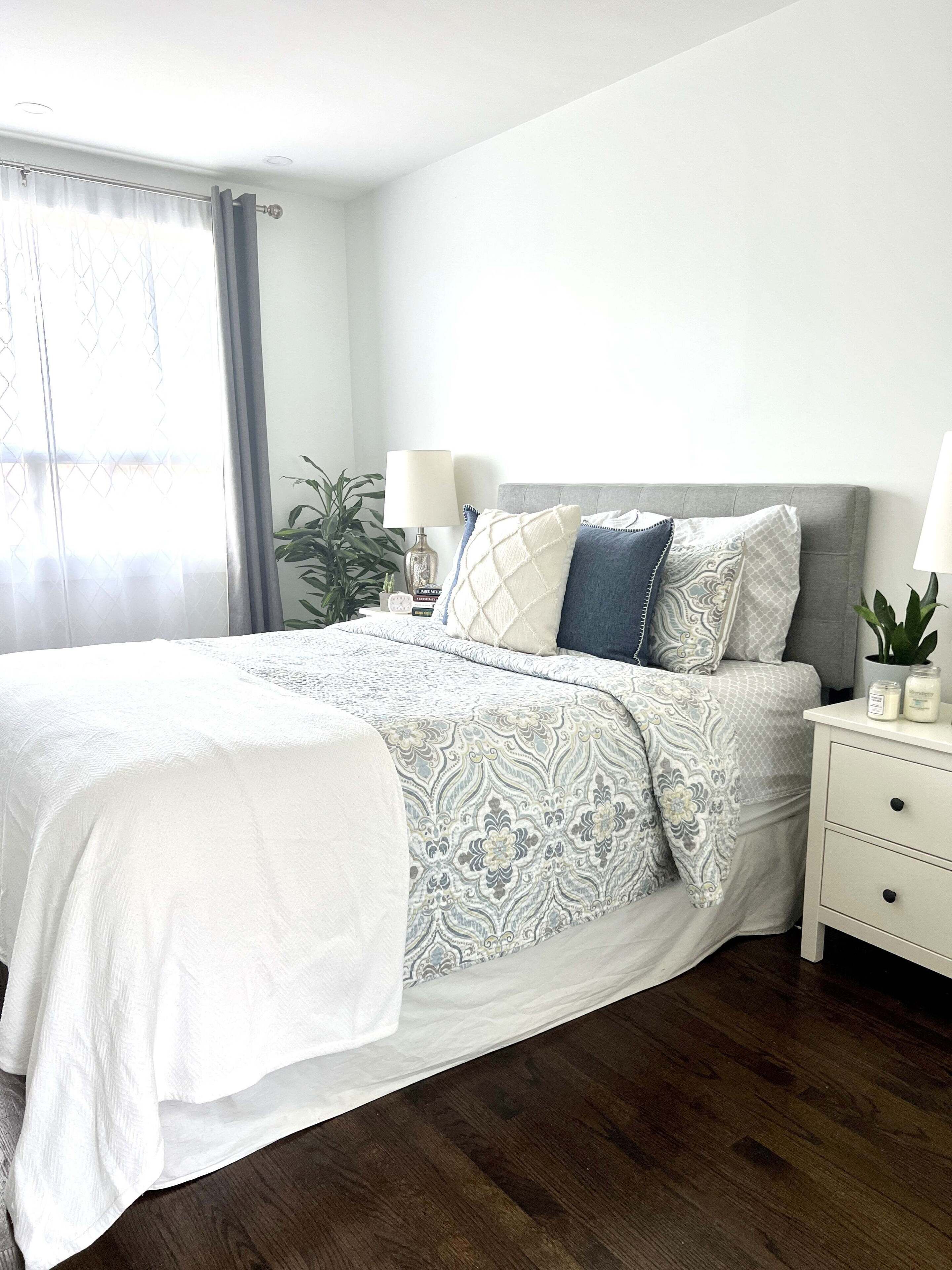 A neatly made bed with a patterned bedspread, a bedside table with a lamp, and a potted plant.