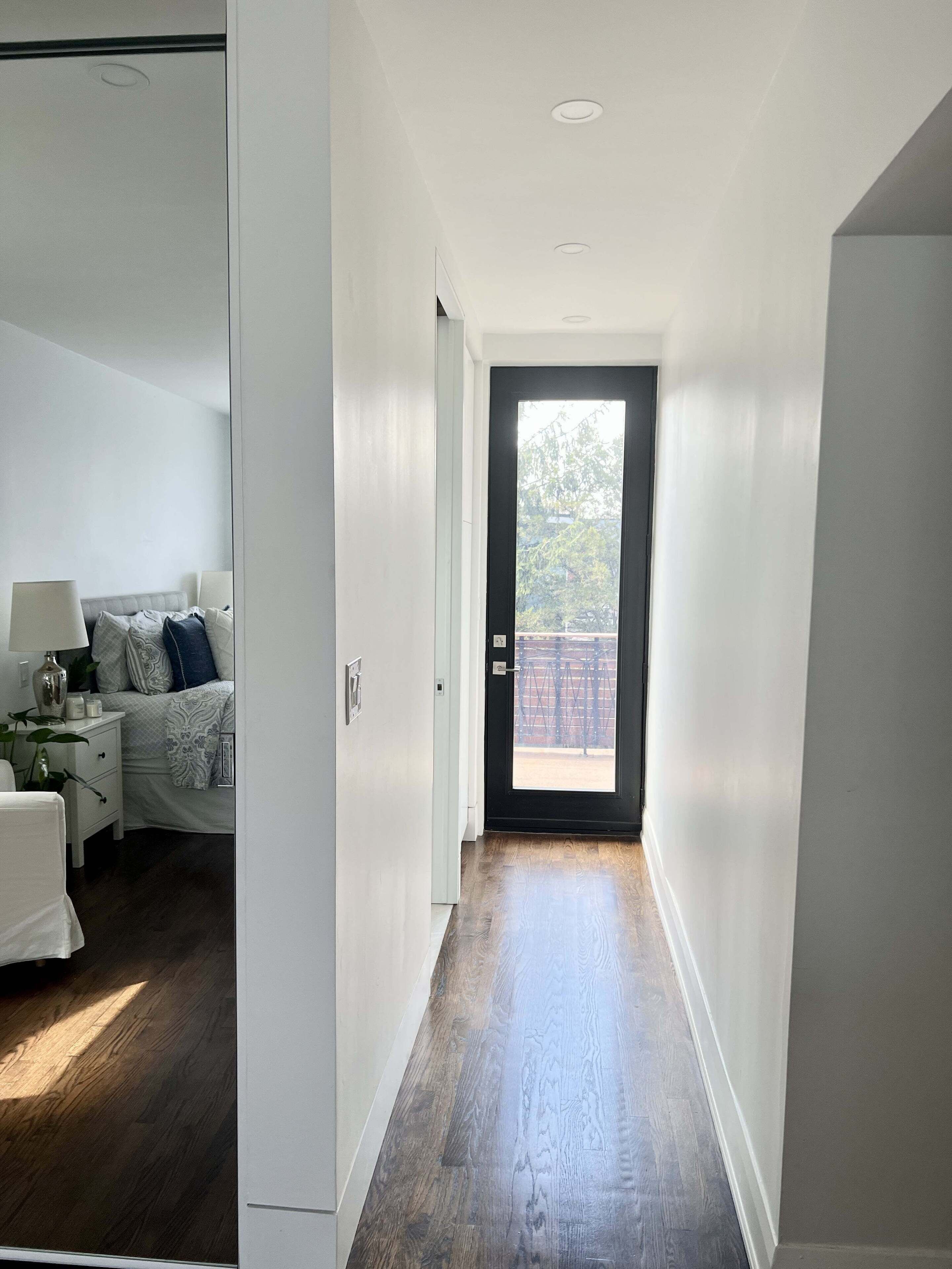 A hallway with a wooden floor leading to a door with a view of a balcony.