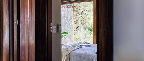 Une chambre à coucher avec un lit, un ventilateur de plafond et une vue sur les arbres, visible à travers une porte coulissante.