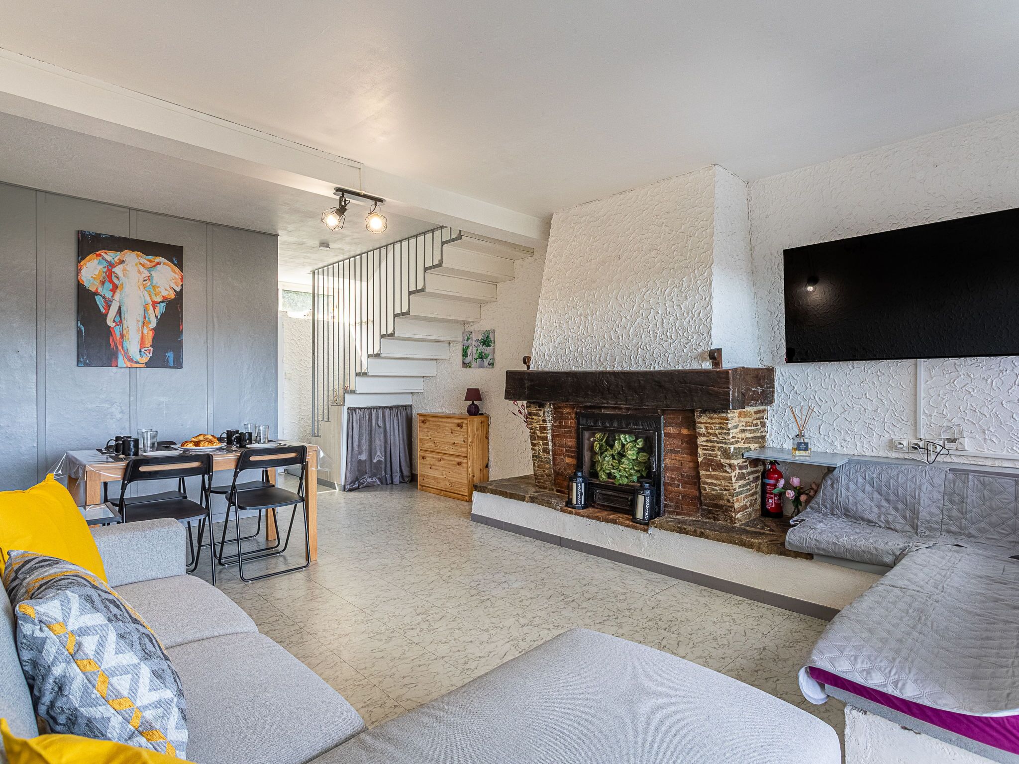 A modern living room with a fireplace, a dining area, and a staircase.