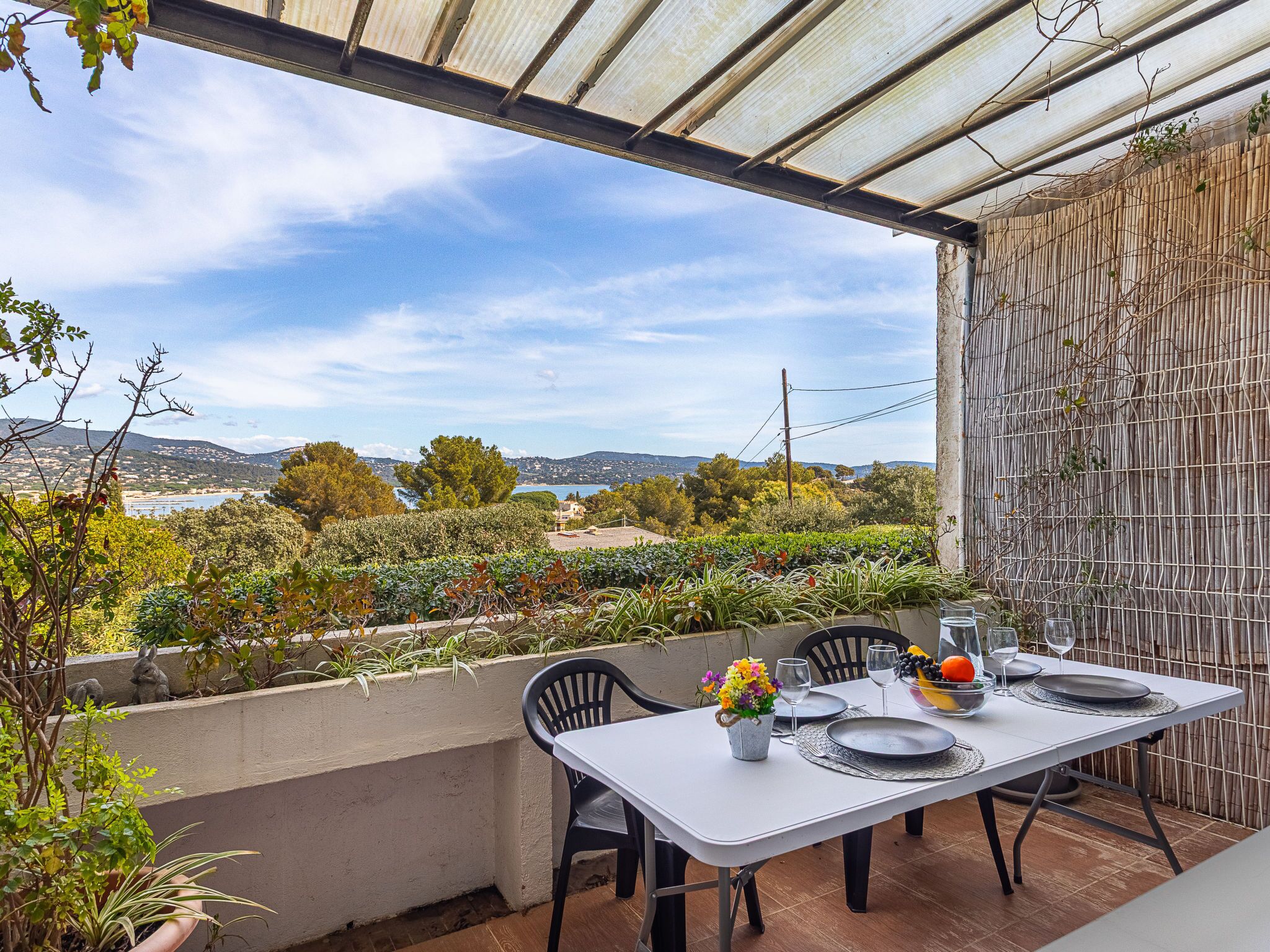 Un área de comedor al aire libre con una mesa dispuesta para dos, con vistas a un paisaje pintoresco que incluye colinas y una masa de agua.