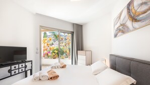 Habitació d'hotel amb llit, televisió, escriptori i finestra amb vista a plantes de colors.