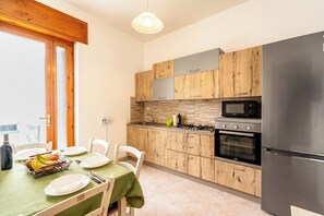 Eine kompakte Küche mit Holzausstattung, einem Edelstahlkühlschrank, einer Mikrowelle und einem Backofen.