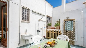 Un patio con una mesa dispuesta para dos, un lavabo blanco y una ventana con celosía metálica.