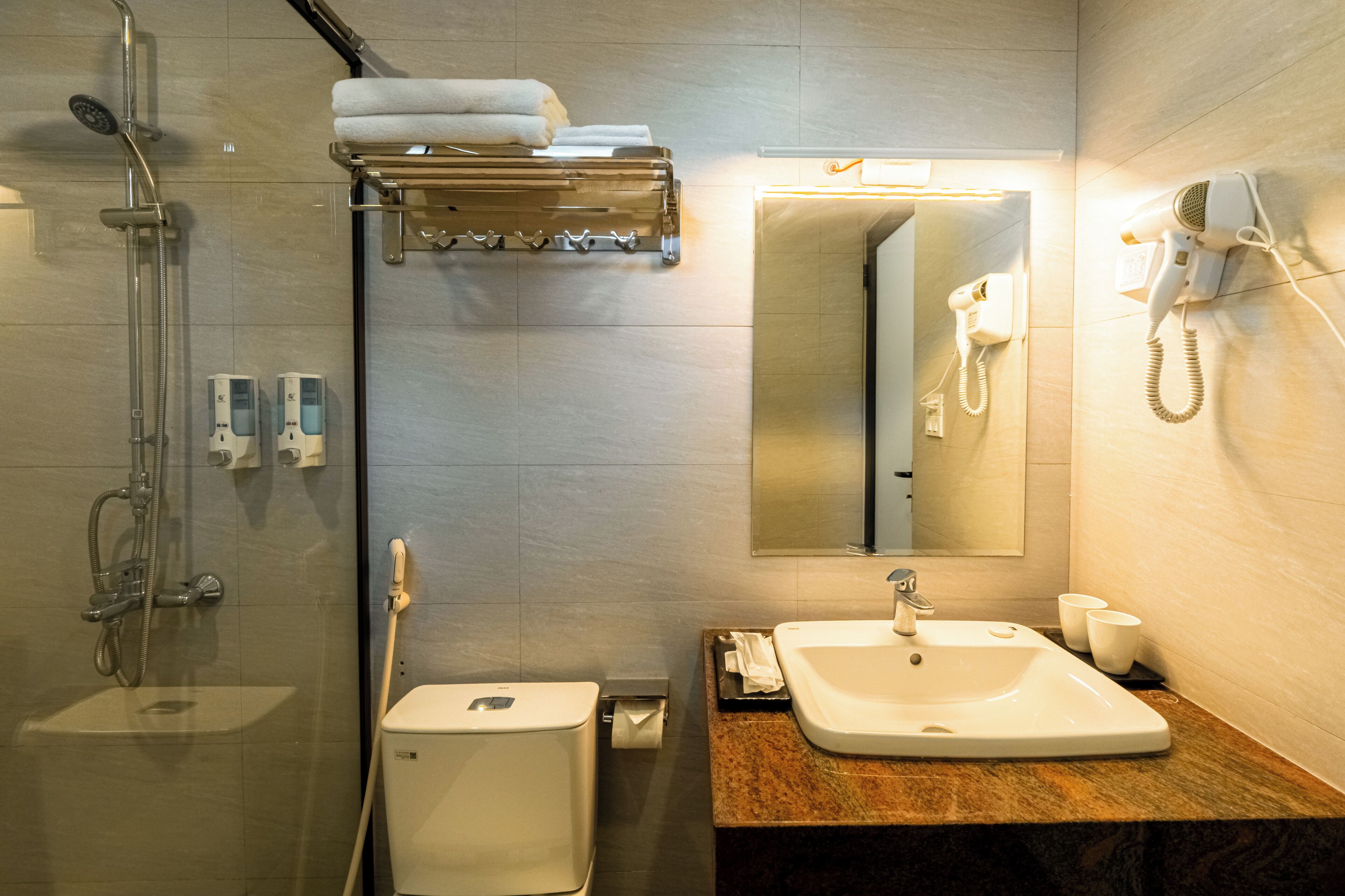 A modern bathroom with a glass-enclosed shower, a toilet, a sink with a mirror, and a hairdryer mounted on the wall.