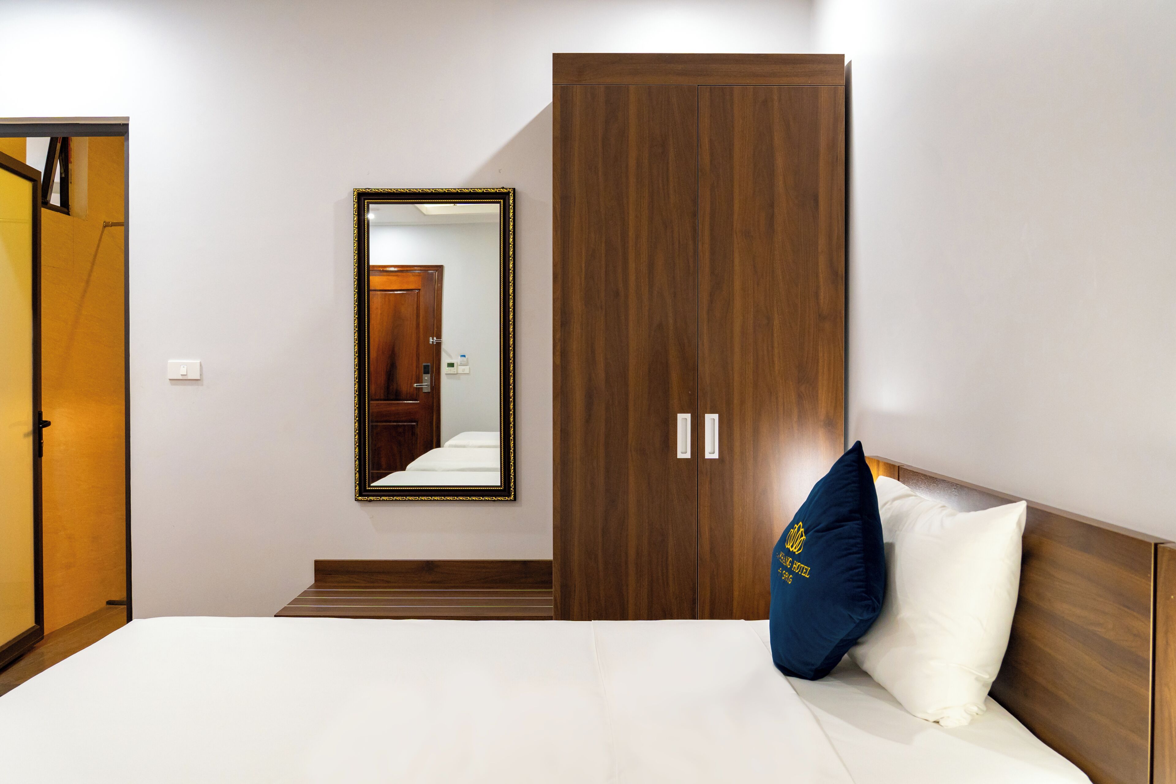 Un dormitorio con una cama, un armario de madera, un espejo y una puerta que da a otra habitación.