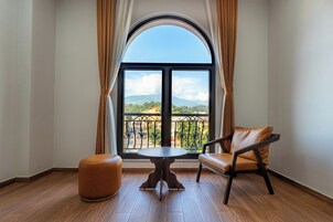 A room with a large arched window, a round table, a leather chair, and a wooden ottoman.