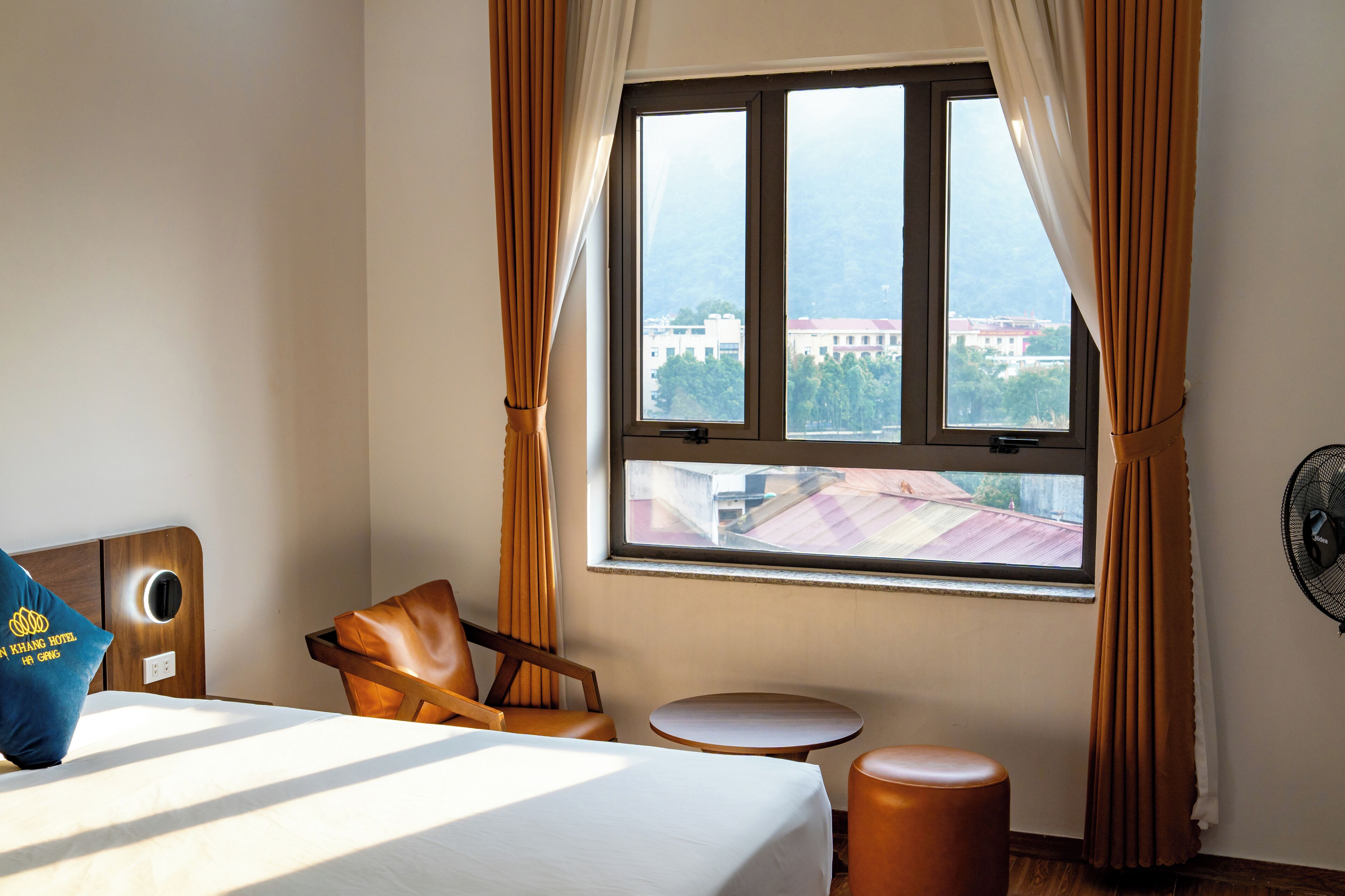 Ein Hotelzimmer mit einem Bett, einem Sessel, einem kleinen Tisch und einem Fenster mit Vorhängen.
