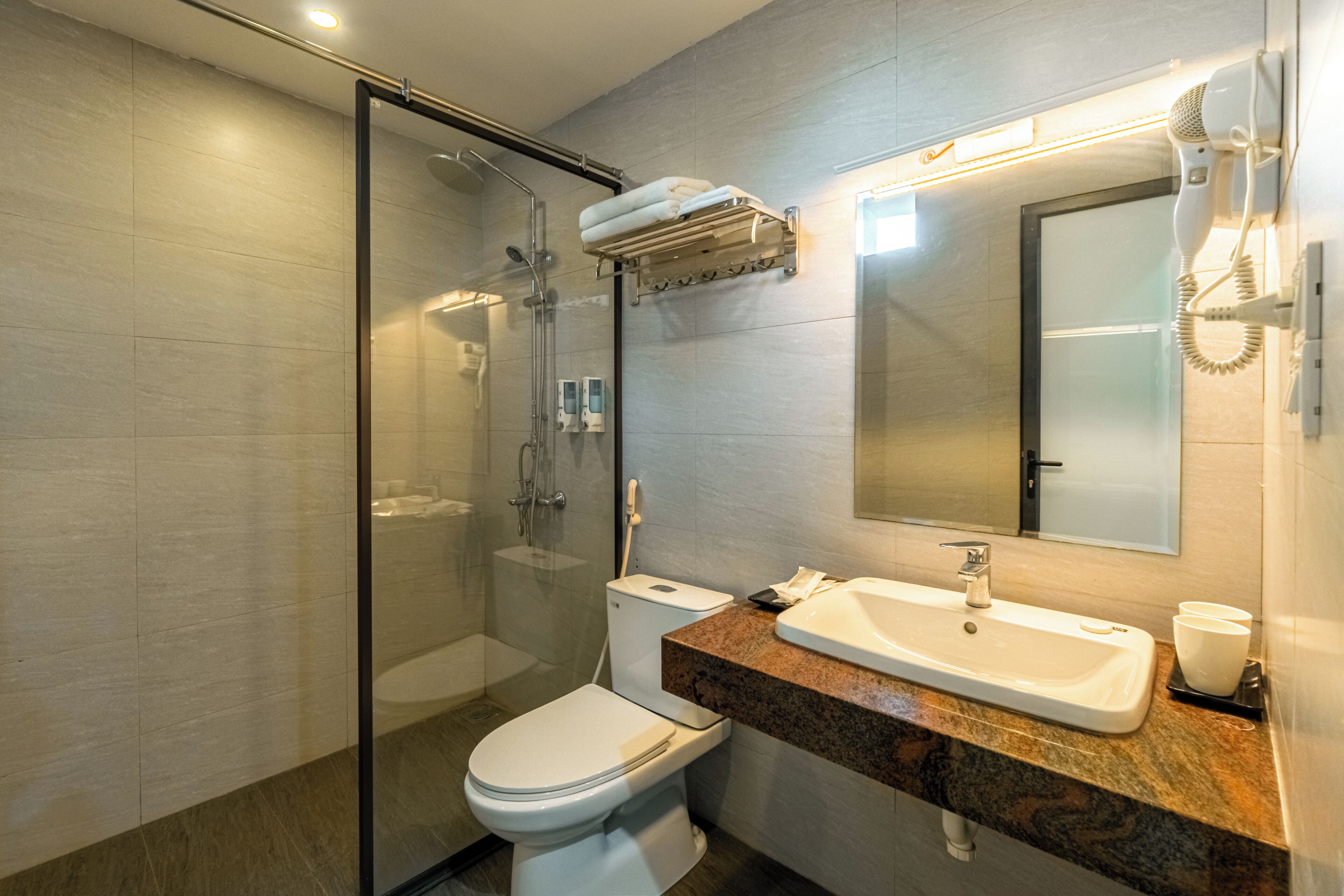 A modern bathroom with a glass shower enclosure, a toilet, a sink with a marble countertop, and a mirror.