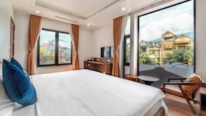 A hotel room with a large bed, a desk, a chair, and a view of buildings through a large window. - An Khang Hotel (Ha Giang 1)