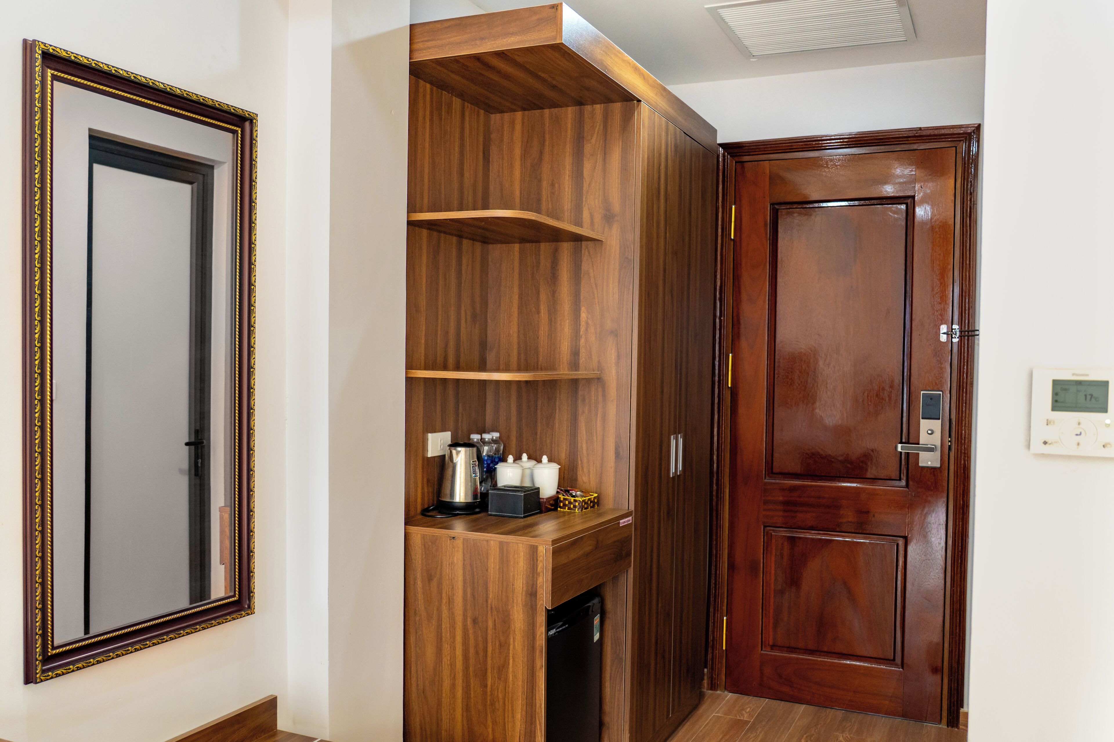 A room with a wooden wardrobe, a mirror, and a door with a digital thermostat.