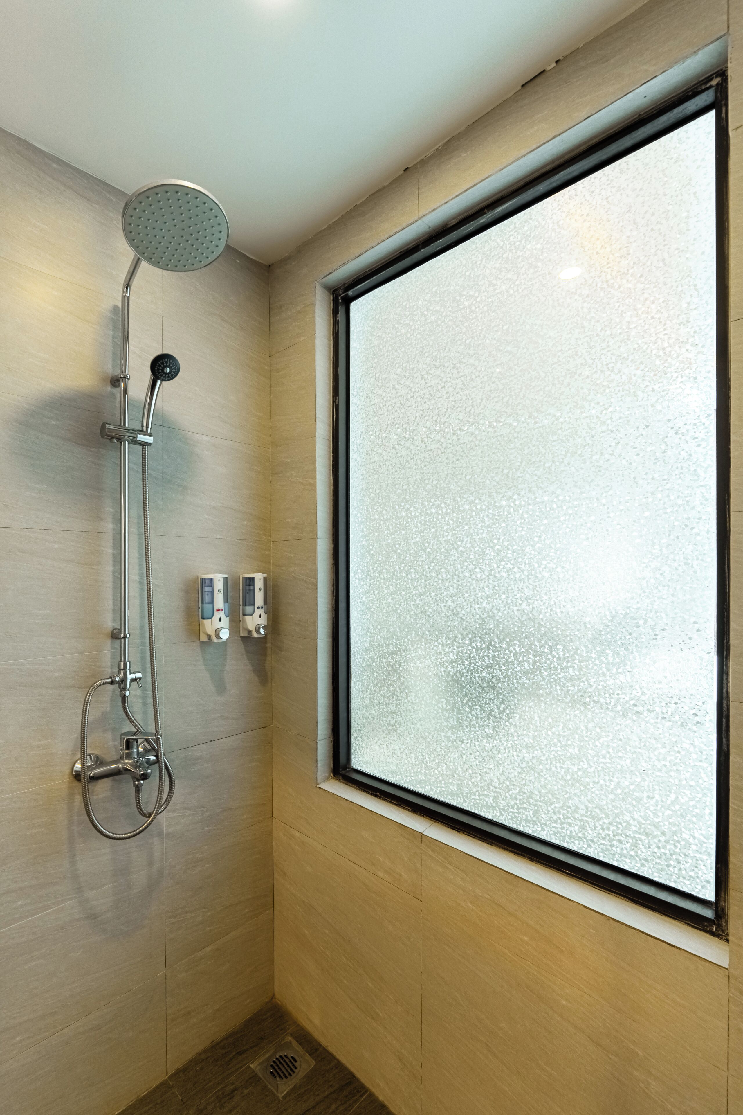 Eine Dusche mit Handbrause, einer fest installierten Bedienfeld und einem Fenster mit Milchglas.