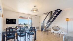 Una sala de estar moderna con comedor, una escalera y vistas amplias por un ventanal.