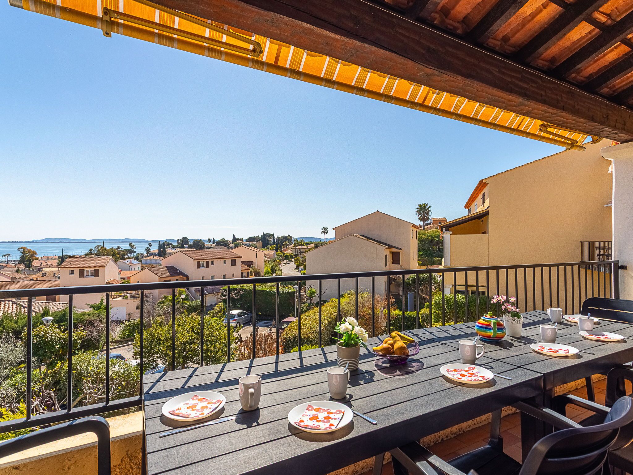 A balcony with a table set for two, overlooking a residential area and the sea.