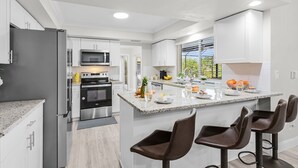 A modern kitchen with stainless steel appliances, a granite countertop, and a central island with bar stools. - Gulf Access Canal home with Pool and Views - Villa Skyline View - Roelens (Cape Coral)