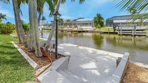 A waterfront property with a dock, palm trees, and a covered area with a view of the water. - Gulf Access Canal home with Pool and Views - Villa Skyline View - Roelens (Cape Coral)