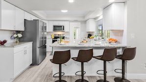 A modern kitchen with white cabinets, stainless steel appliances, and a central island with bar stools. - Gulf Access Canal home with Pool and Views - Villa Skyline View - Roelens (Cape Coral)
