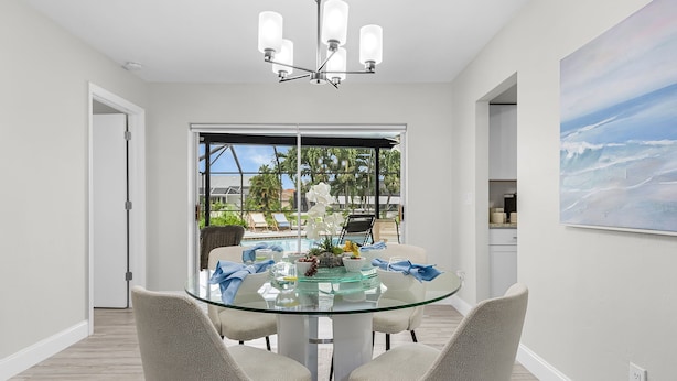 A modern dining area with a glass table, four chairs, and a chandelier. - Gulf Access Canal home with Pool and Views - Villa Skyline View - Roelens (Cape Coral)