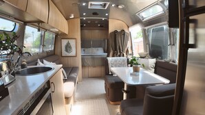 A compact RV interior with a kitchenette, seating area, and a bed. - Charming Airstream Wellness Retreat in Wine Country (Fairfield)