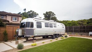 A stationary RV parked in a backyard with a well-maintained lawn, a wooden fence, and a house in the background. - Charming Airstream Wellness Retreat in Wine Country (Fairfield)