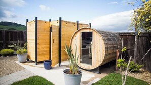 A wooden sauna structure with a curved door, surrounded by a wooden fence, and potted plants in the foreground. - Charming Airstream Wellness Retreat in Wine Country (Fairfield)