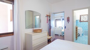 A bedroom with a bed, a dresser, a mirror, and a bathroom visible through an open door. - Apartment 'Casa Vacanze Ribes' with Sea View, Shared Pool and Private Terrace (olbia)