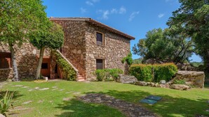 A stone house with a stone staircase leading to the entrance, surrounded by a well-maintained lawn and trees. - Apartment 'Casa Vacanze Ribes' with Sea View, Shared Pool and Private Terrace (olbia)