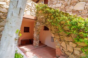 A stone archway with greenery, a tree trunk, and a small wooden bench.