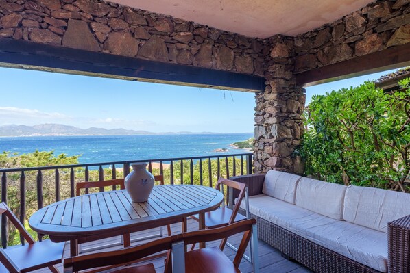 A stone-framed balcony with a table and chairs, a sofa, and a view of the ocean.