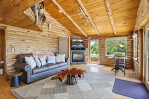 A log cabin interior with a fireplace, a sofa, a coffee table, and a dining area.