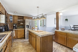 A spacious kitchen with wooden cabinets, granite countertops, stainless steel appliances, and pendant lighting.