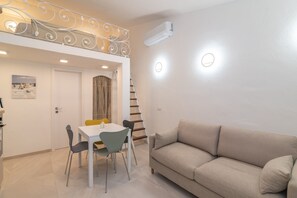 Ein Wohnbereich mit einer Couch, einem Esstisch, Stühlen, einer Treppe und einer Klimaanlage.