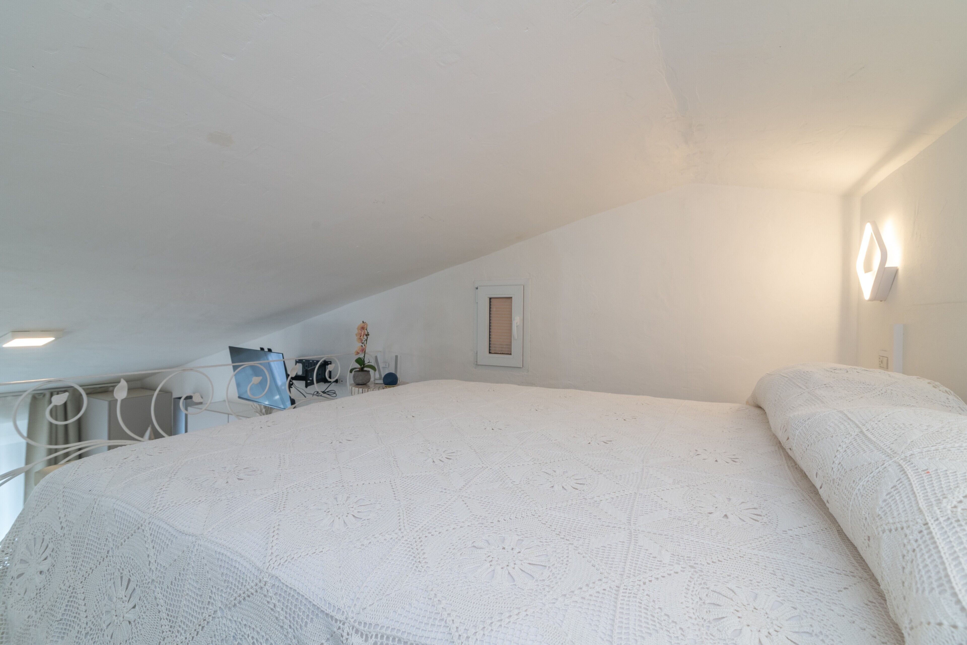 Un dormitorio con una cama grande, una ventana pequeña y una lámpara de pared.