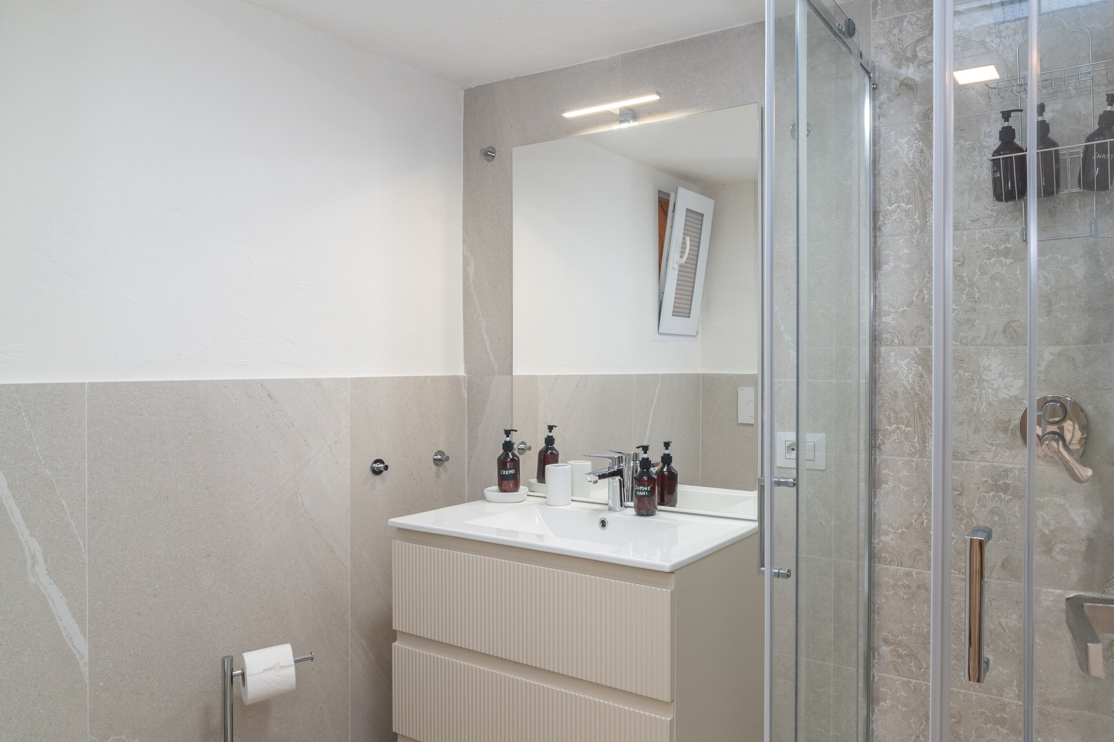 Une salle de bain moderne avec une douche à parois de verre, un lavabo blanc avec un miroir au-dessus et un porte-serviettes.