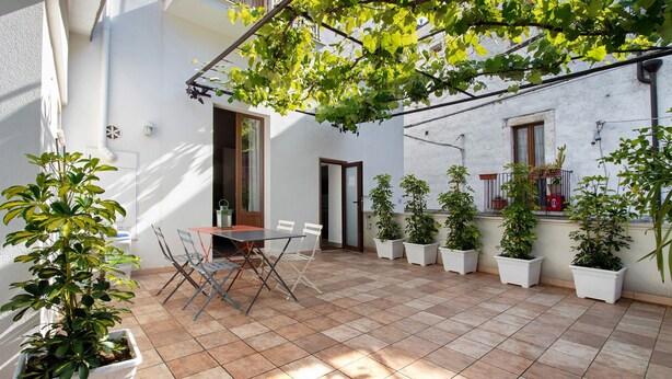 A courtyard with a tiled floor, a table with chairs, potted plants, and a pergola with greenery. - Apartment 'Unit 1' with Shared Terrace, Wi-Fi and Air Conditioning (Rutigliano)