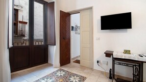 A hallway with a patterned rug, a wooden door, a white door, a mounted TV, and a small table with a cloth. - Apartment 'Unit 1' with Shared Terrace, Wi-Fi and Air Conditioning (Rutigliano)