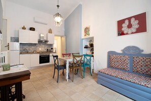 Una cocina compacta con armarios blancos, una mesa de comedor con sillas y un sofá azul con cojines estampados.