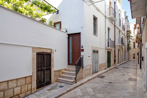 Una calle estrecha flanqueada por edificios, una puerta de madera y una reja de metal.