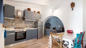 A compact kitchen with a tiled backsplash, modern appliances, and a dining area with a table and chairs. - Apartment 'Unità Due' with Shared Terrace, Wi-Fi, and Air Conditioning (Rutigliano)
