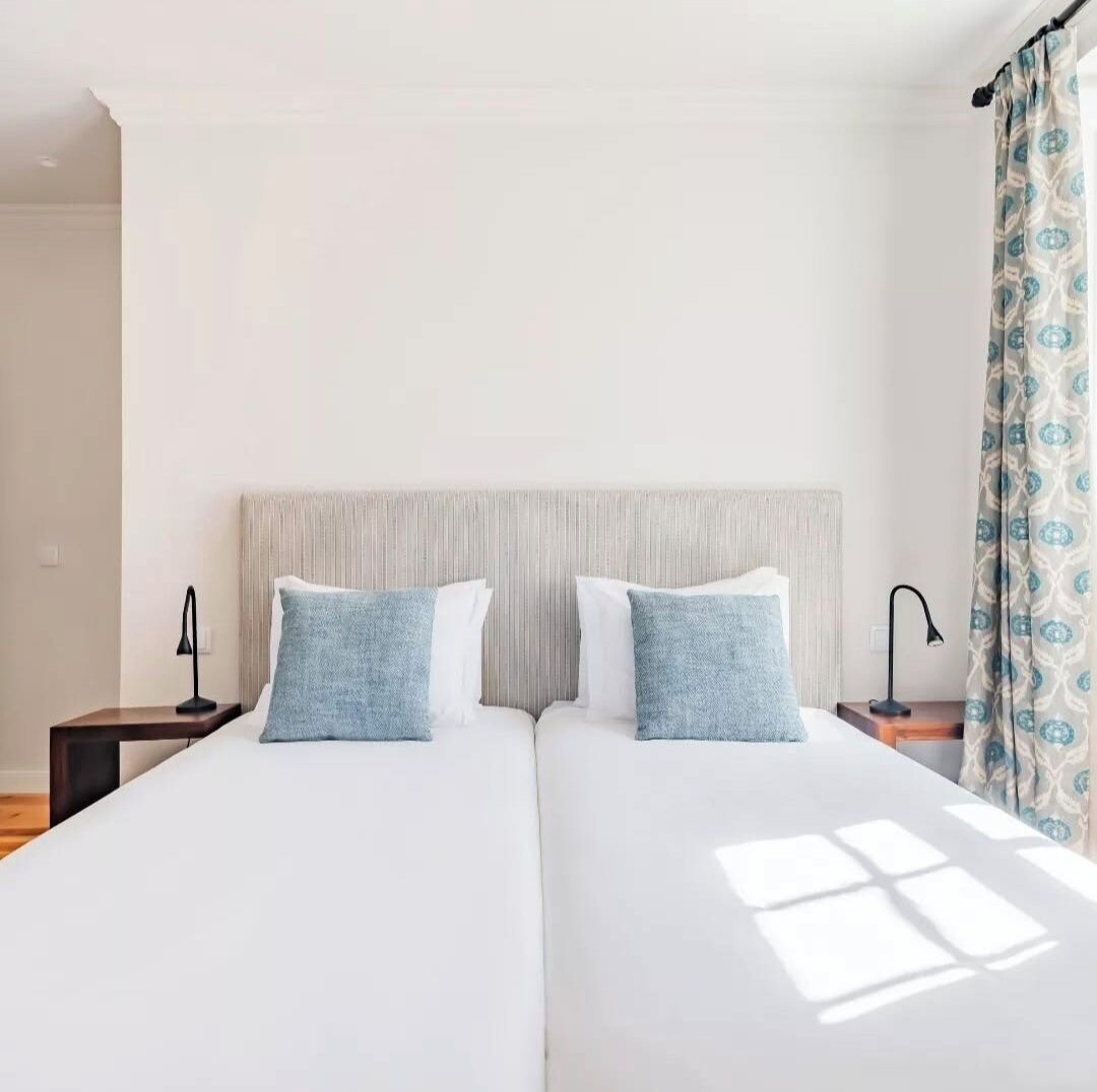 Una cama doble con cabecera a rayas, dos mesitas de noche con lámparas y una ventana con cortinas.