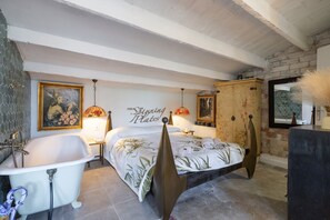 Un dormitorio con una cama grande, una bañera antigua, un armario de madera y una pared con un cuadro y texto.