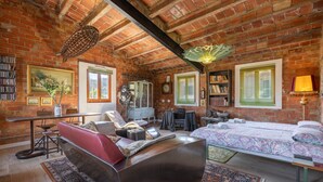 A room with exposed brick walls, a bed with patterned bedding, a red sofa, a wooden coffee table, a desk with a chair, and a bookshelf. - Apartment 'La Fabriqueta Deluxe' with Mountain View, Wi-Fi and Air Conditioning (Riudecanyes)
